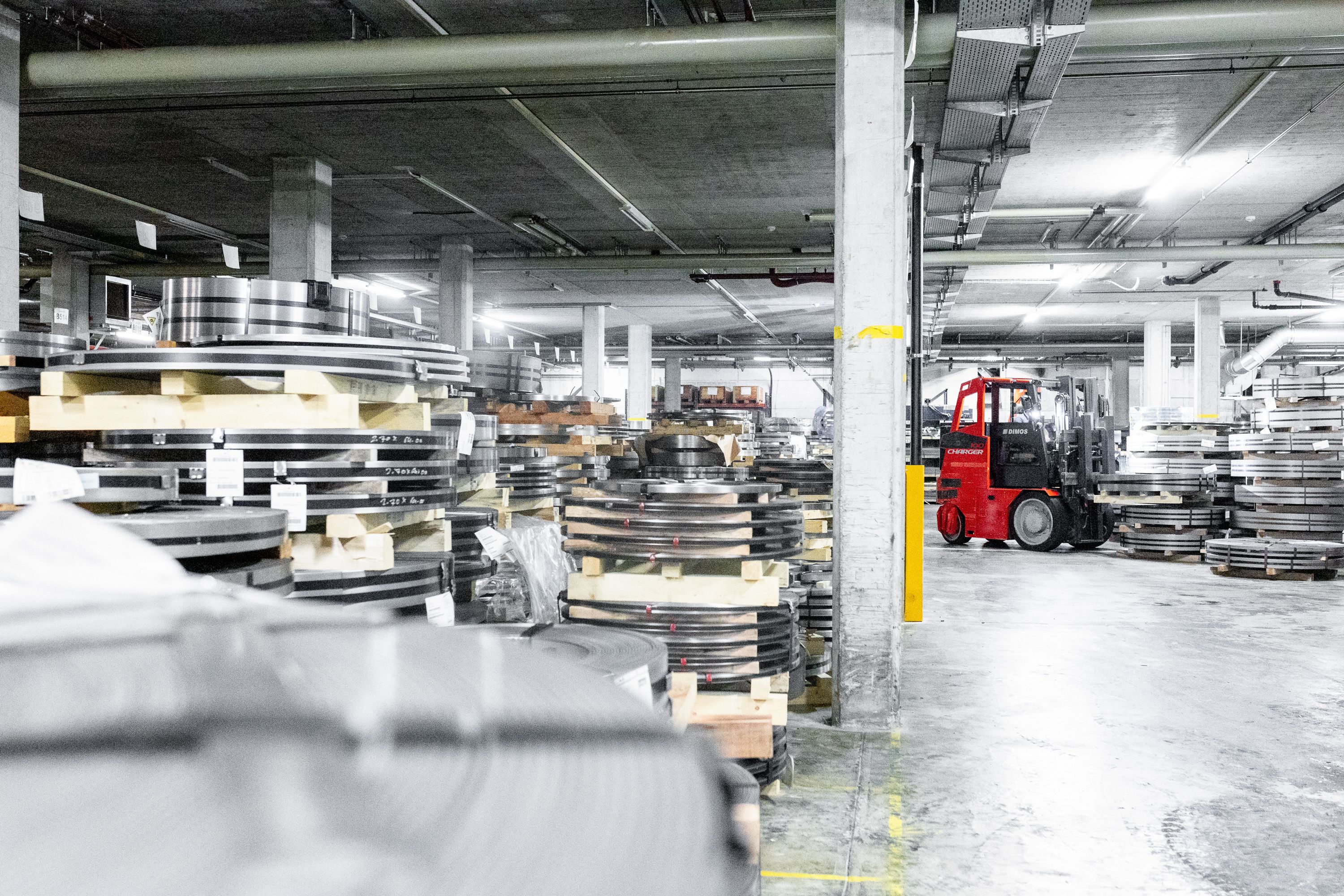 Dimos Charger100 Schwerlaststapler transportiert Metallcoils in Industriehalle – B2B Fotoproduktion für Schwerlasttechnik.