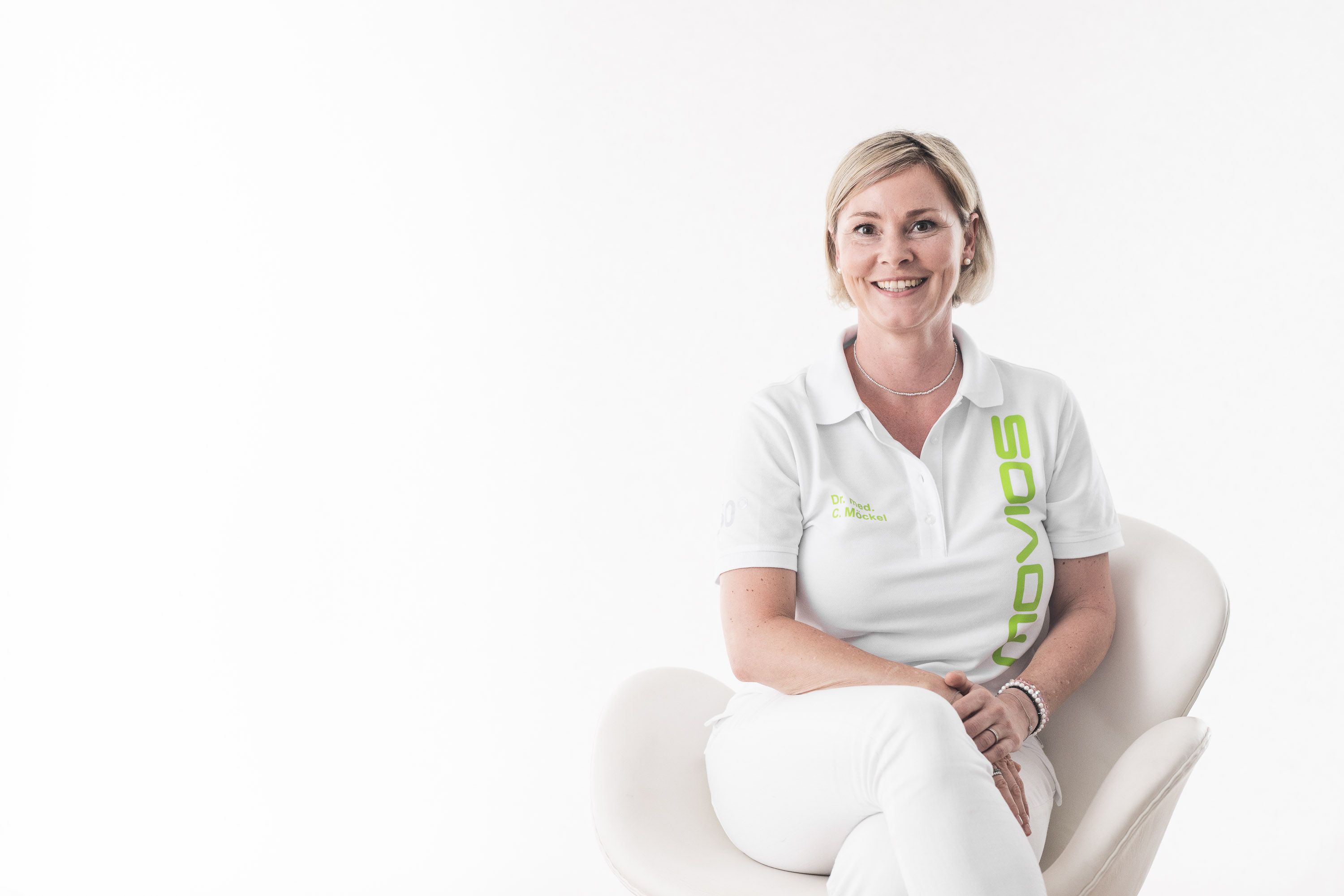 Ärztin sitzt auf Stuhl - Modernes Portrait bei Fotoshooting für Praxen mit weißer Wand