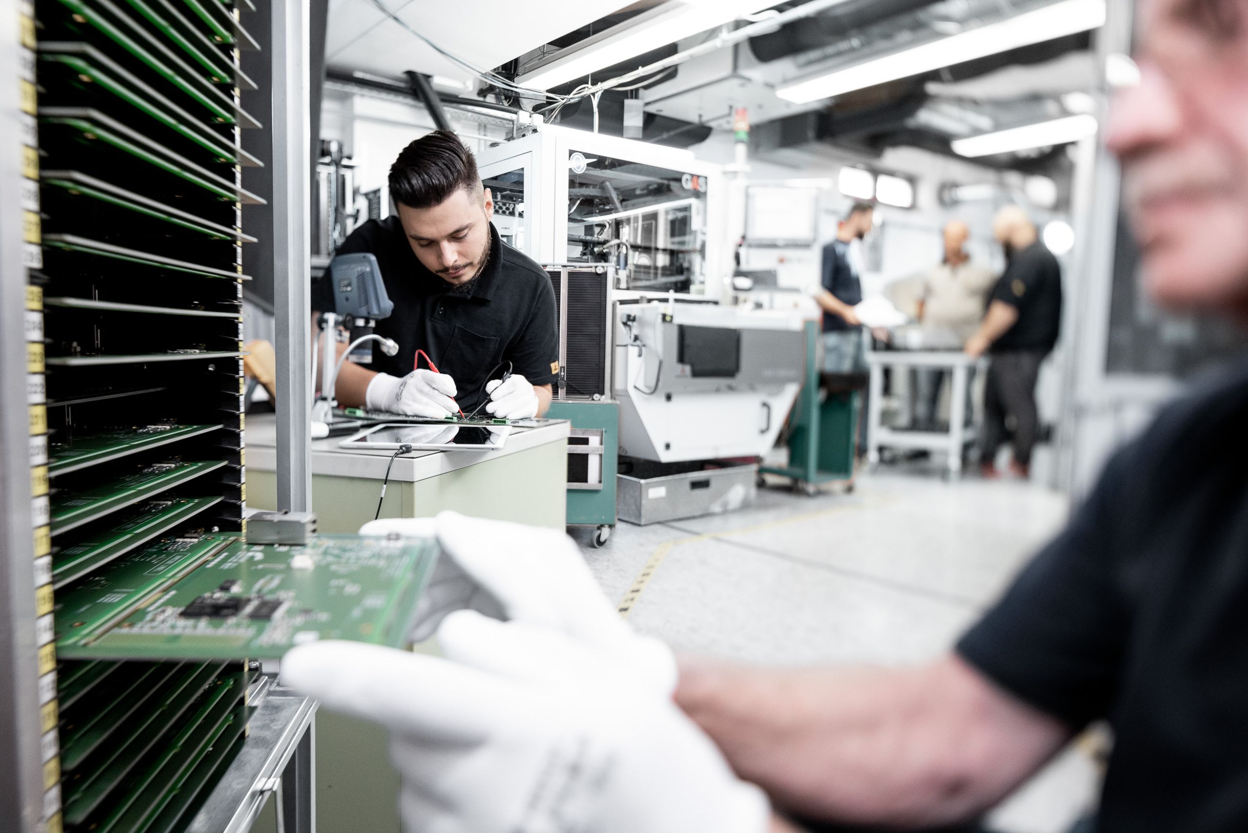 Contentproduktion für CI & Rebrand - Platine wird in einen Tray geschoben, Mitarbeiter überprüft Spannung in der Produktion