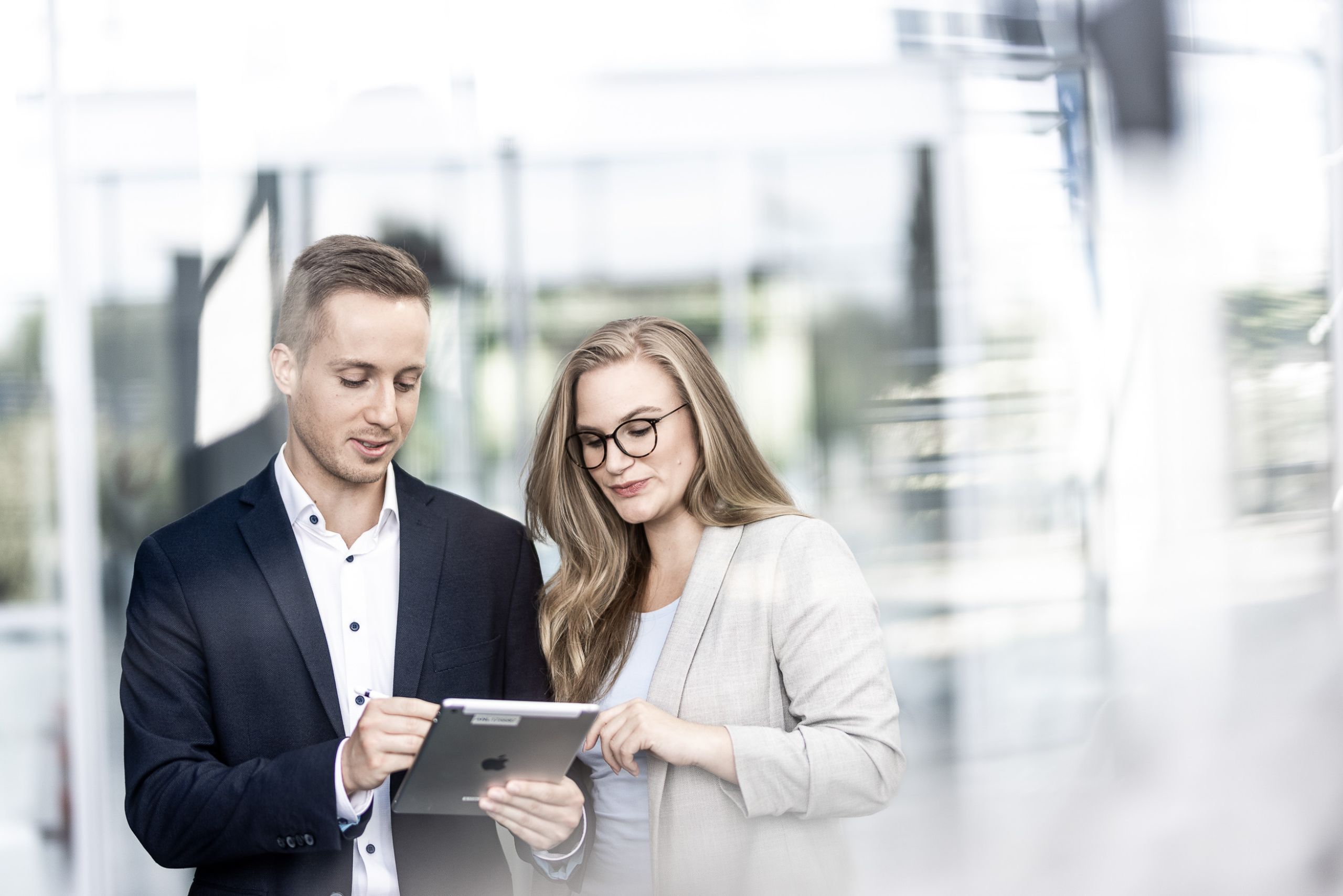 Imagefotografie für Unternehmen in Frankfurt - 2 Personen stehen hinter Glasscheibe in moderner Location und schauen sich etwas auf dem IPAD an