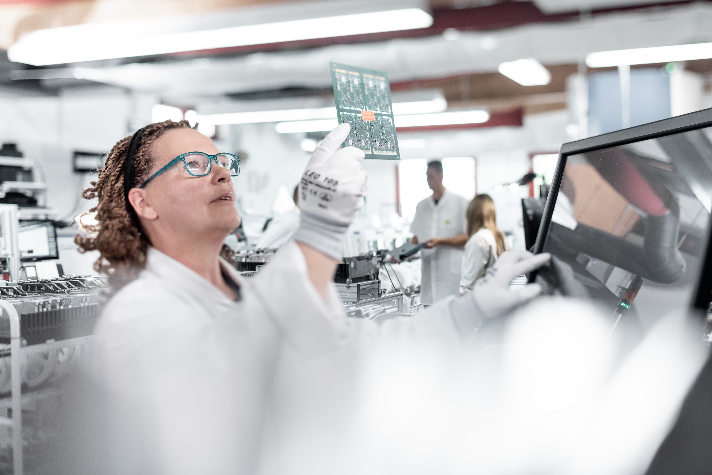 Werbeaufnahmen in einem Labor - Mitarbeiterin schaut akribisch und motiviert eine Platine an in ESD umgebung mit Handschuh