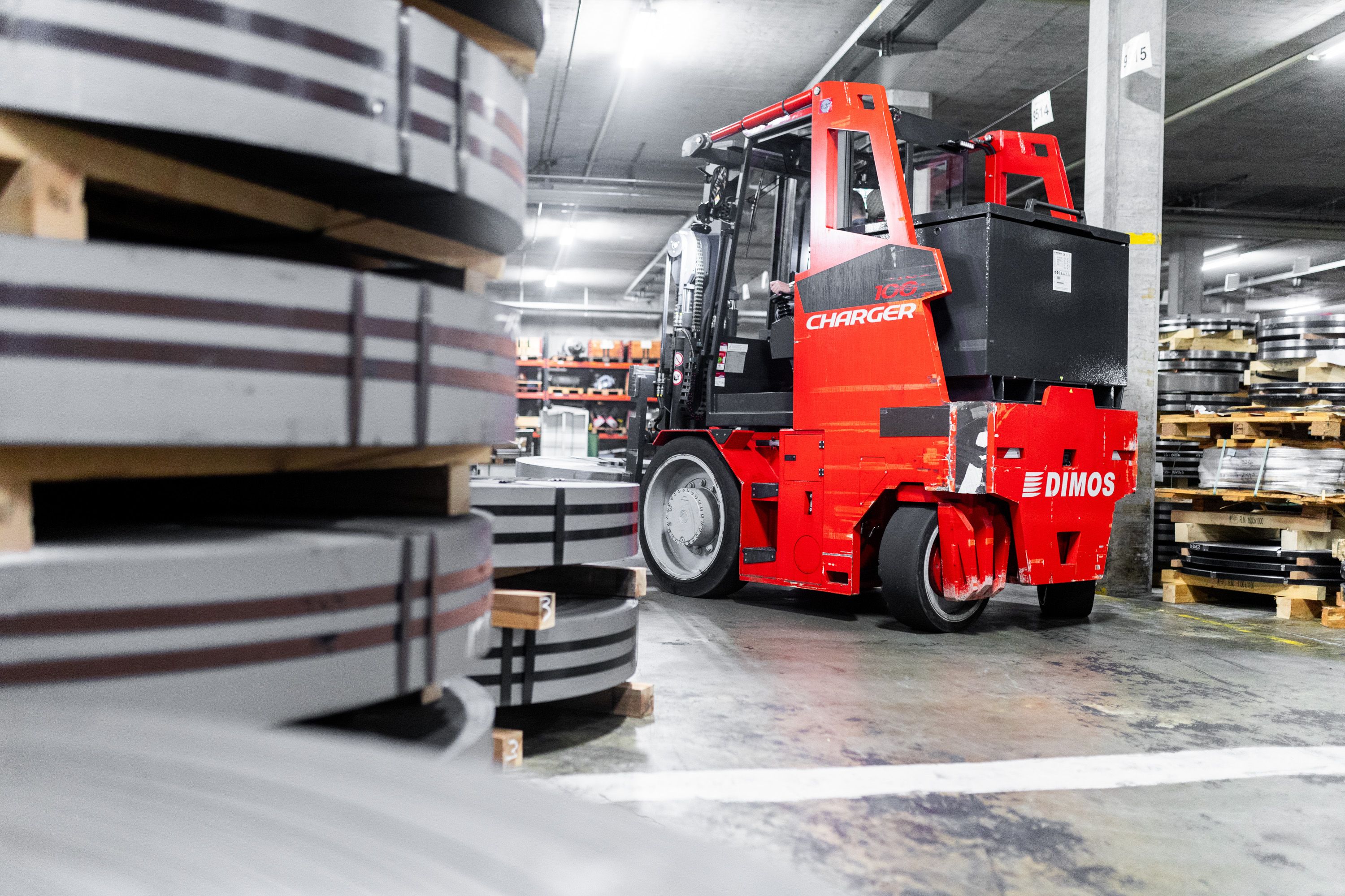 Dimos Charger100 beim Handling von schweren Metallspulen – Industriefotografie für Lagerlogistik.